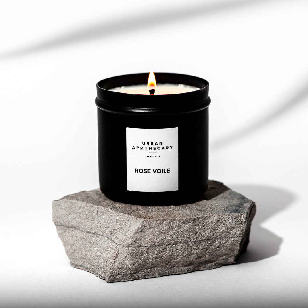 Candle in a black container labeled 'Urban Apothecary' on a stone surface with a white background